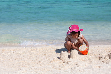 Cute asian child girl having fun to play with sand on beach in summer vacation