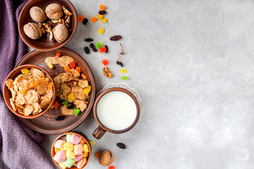 Morning still life. Healthy breakfast (wheat flakes, walnuts, candied fruits, raisins, milk) on a gray textured background.