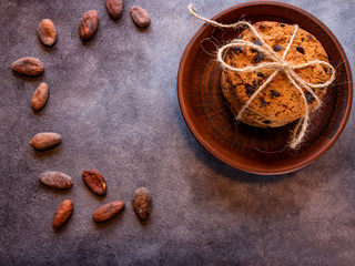 Chocolate cookies in a clay plate, stacked, tied with a rope and cocoa beans, on a textured background. Close-up