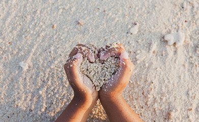 Child girl holding sand make heart shape in hands and playing on the beach in summer vacation