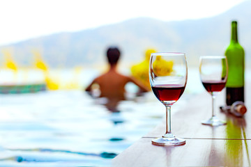 Two glasses of red wine near the swimming pool with a man is swimming in the pool