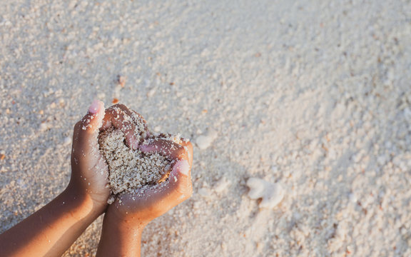 Child girl holding sand make heart shape in hands and playing on the beach in summer vacation