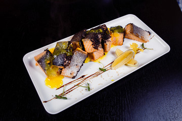 Honey Glazed fillet salmon with orange slices, spices and basil on white plate on dark background.