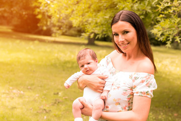 A young mother standing in the park and holding her baby