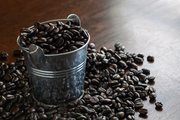 Coffee beans in a small bucket with some spreading on the wooden table