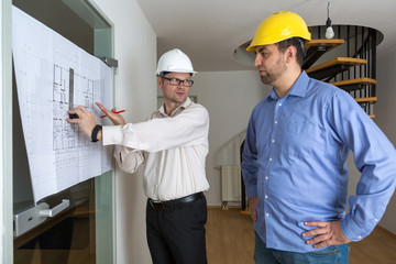 Architekt mit weißem Helm und Bauherr mit gelbem Helm besprechen Details des Bauplans
