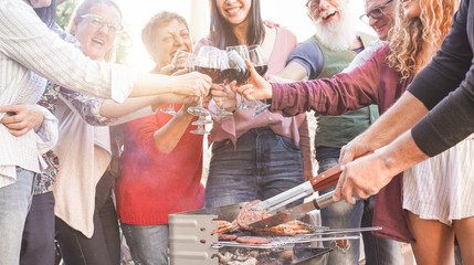 Family grilling meat and cheering with red wine at bbq meal outdoor - Focus on hands toasting