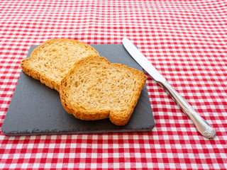 Two slices of toast on a slate plate, one knife and tablecloth vintage style