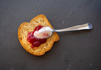 A spoon with raspberry jam on a slice of toast on a plate slate