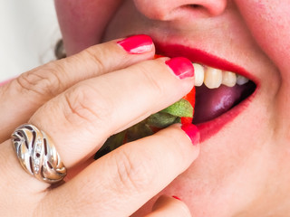 An adult woman with red nails and lips eating a strawberry