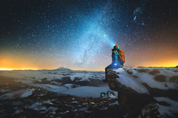 Night winter landscape a man with a backpack and a lantern on his head sits on a rock in the...