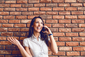 Portrait of attractive brunette talking on the phone while sitting in cafeteria. In background brick wall.