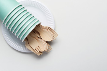 Wooden single use kitchenware and paper cups and plates on white. Top view
