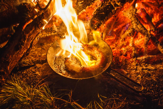 Adding sausages in a pan on a fire in the night forest