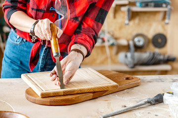 Woman carpenter with chisel finishing work with wooden cutting board. Art and useful hobby concept