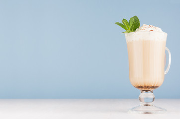 Cappuccino coffee with whipped cream, green mint, cocoa powder in  transparent glass with handles...