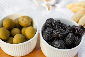 set of three white bowls with olives on wooden tray on white blanket