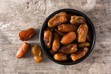 Dates in black bowl on wooden table. Top view