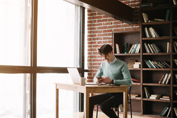 Young handsome student typing on his notebook his diploma. Student discussing on the phone universities's timetable. Education online. Work on freelance. Software development.