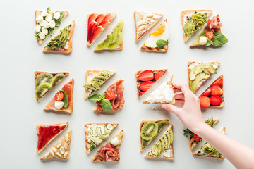 cropped view of woman holding slice of bread over toasts with fruits and vegetables isolated on white