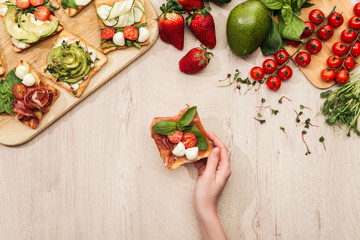 top view of woman with delicious vegetable toasts and fresh ingredients on wooden table