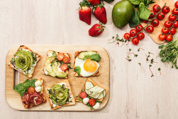 top view of toasts with vegetables on chopping board and fresh ingredients on wooden table