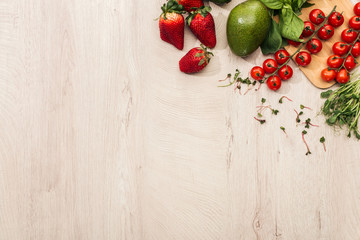 Fototapeta na wymiar top view of strawberries, cherry tomatoes, avocado and basil on wooden table with copy space