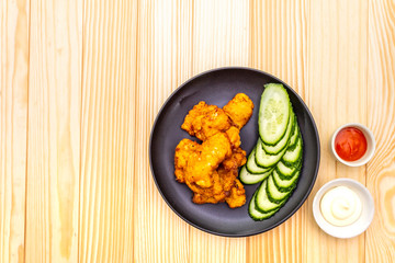 Chicken fried (nuggets) homemade on black plate with two sauces - mayonnaise and hot spicy sauce. On wooden background, top view