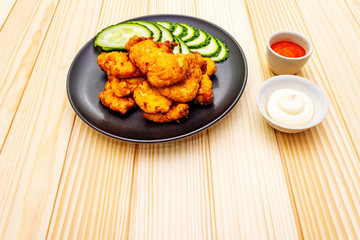 Chicken fried (nuggets) homemade on black plate with two sauces - mayonnaise and hot spicy sauce. On wooden background