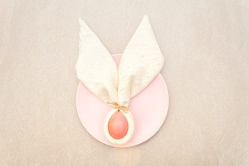 Easter bunny (rabbit) egg concept, table arrangement decoration. Pink (rosy) eggs with plate, cloth vintage linen napkin on a stone background, top view