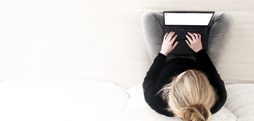 top view of young woman cross-legged sitting on sofa working on laptop computer