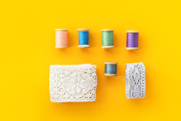 Knolling sewing crafts hobbies fashion clothing background with white cotton lace rolls wooden vintage spools with multicolored threads on bright yellow backdrop. Poster streamer placeholder template