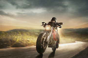 Speed of inspiration, aspiration and wild energy on the road. Get faster. Biker in black helmet is driving the handsome sport motorbike near meadows and mountains in cloudly evening on country side. - obrazy, fototapety, plakaty