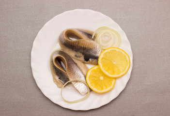 marinated herring fillet with onion and lemon on white plate, top view with copy space