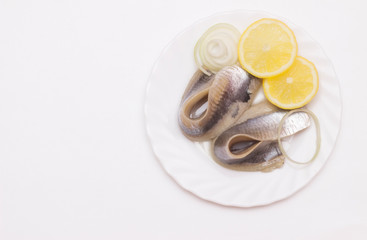 marinated herring fillet with onion and lemon on white plate, top view with copy space