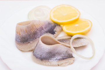 marinated herring fillet with onion and lemon on white plate, top view with copy space