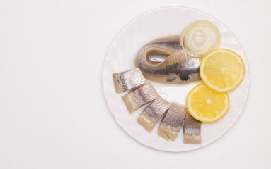 marinated herring fillet with onion and lemon on white plate, top view with copy space