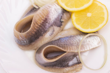 marinated herring fillet with onion and lemon on white plate, top view with copy space