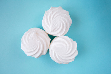 Three white lush fresh marshmallows on a bright blue monochrome background close-up at the center of the frame