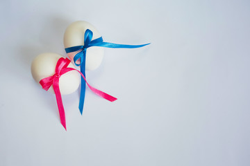 two identical white eggs tied with pink and blue ropes on a light background symbolize the identical twins of a boy and a girl with free space on the right