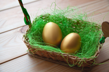 two golden eggs in wicker basket, on wooden background. Easter