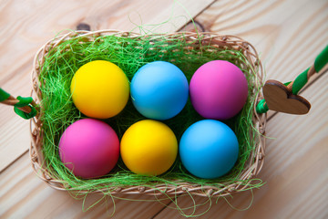 Colorful easter eggs in basket, on wooden background. Top view
