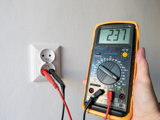 Hand holding an electric multimeter in front of the electric socket