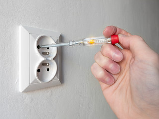 Hand holding an electricity tester and checking voltage in electric socket