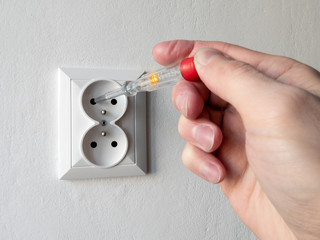 Hand holding an electricity tester and checking voltage in electric socket