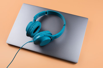 Photo of stylish modern computer or notebook and blue cyan headphones over beige background.