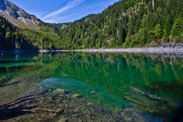 Turquoise water of a mountain lake surrounded by green wooded hills under a blue sky. Lake Ritsa...