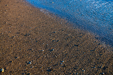 Sand and stones on the seashore after a surging wave in the sunset rays of the sun. background image. Tourism in Abkhazia.
