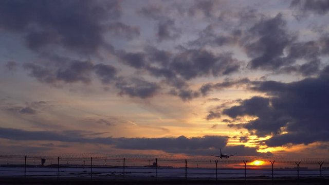 Plane is landing. Past rides a truck and aircraft tug. Sunset, blue sky, purple and orange clouds in the background. Good weather. 4K stock footage