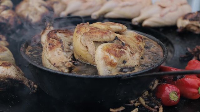 Slow motion pan shot right to left of cooking or frying chicken in boiling hot oil in cast iron kazan in open space. Chicken thighs fried in kettle during street food market